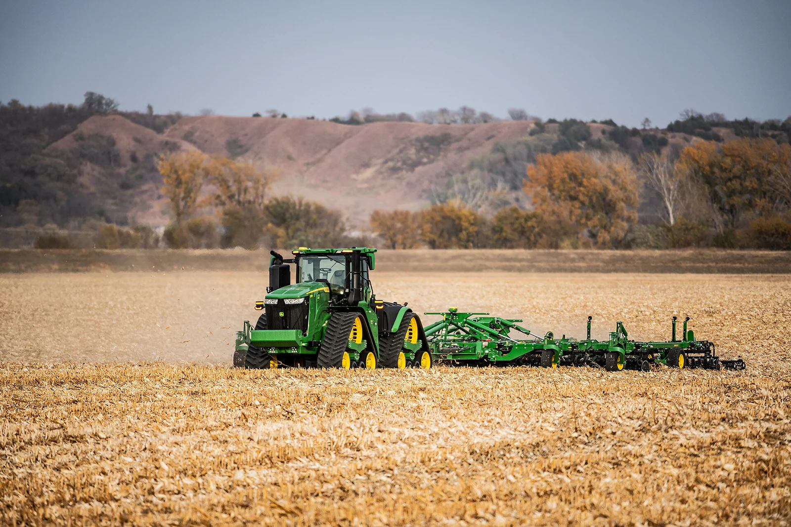 넓은 농지에서 경운 작업기를 끌고 이동하는 John Deere 트랙터